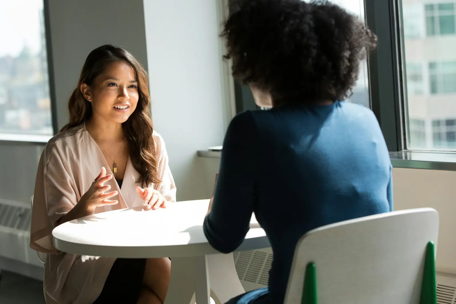 Two women talking across a small table in a bright office
